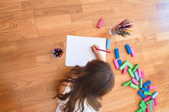 Adorable toddler lying down on the floor drawing using paper and pencils at kindergarten