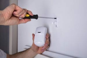 Close-up Of A Young Male Electrician Installing Security System Door Sensor On Wall