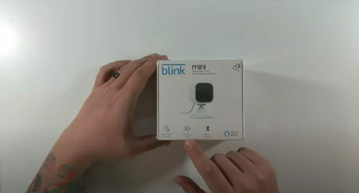 a man's hand holding a box of mini blink camera