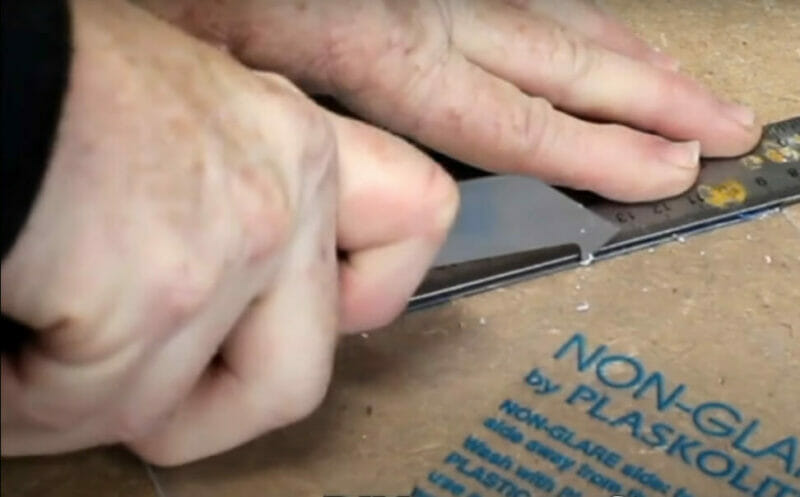 A person cutting a portion of a Plexiglass