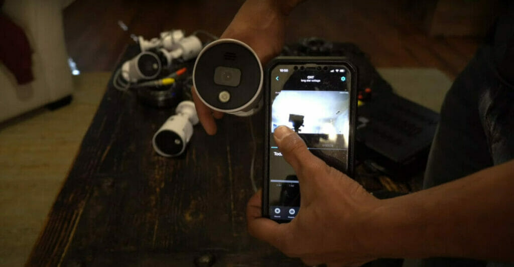 A person capturing an image of a camera on a table as part of an easy steps guide for installing Night Owl wired security cameras